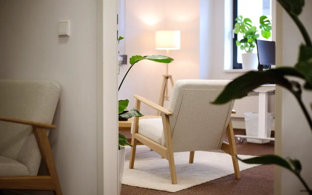 Blick durch die Tür in einen Therapieraum der Praxis am Berliner Tor in Hamburg: heller Sessel, Stehlampe und Pflanzen