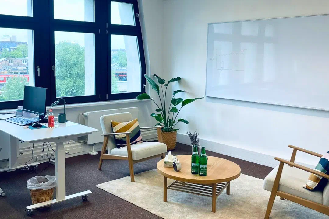 Therapieraum der Praxis am Berliner Tor mit zwei Sesseln, rundem Tisch und Blick aus den großen Fenstern über die Gleise